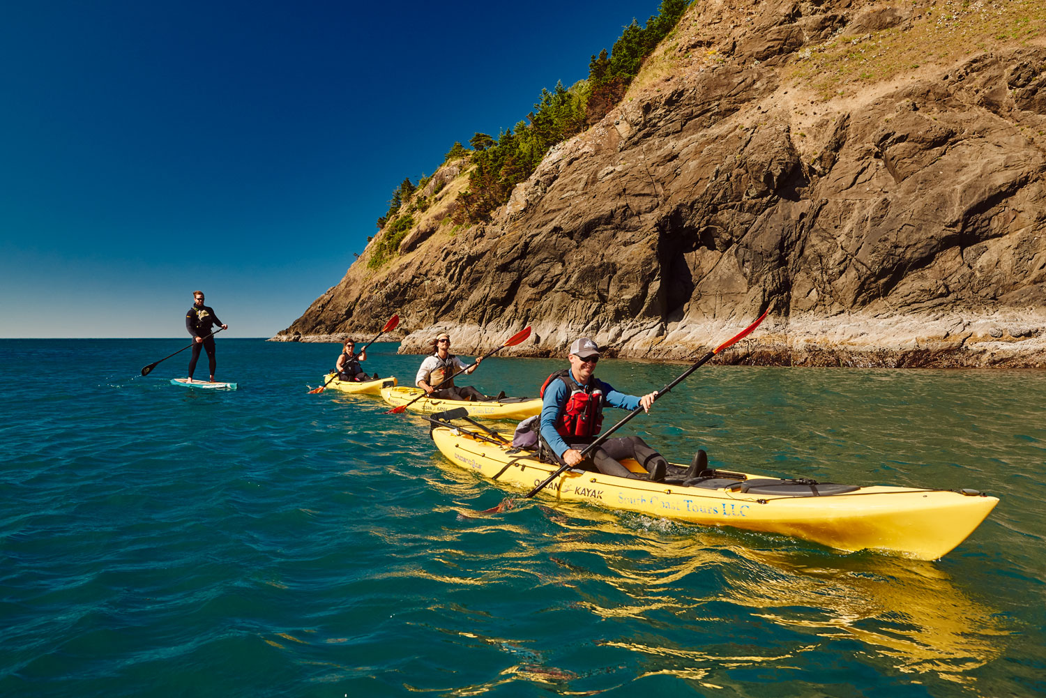 kayakers and a paddle boarder paddling along rocks near Port Orford, Oregon